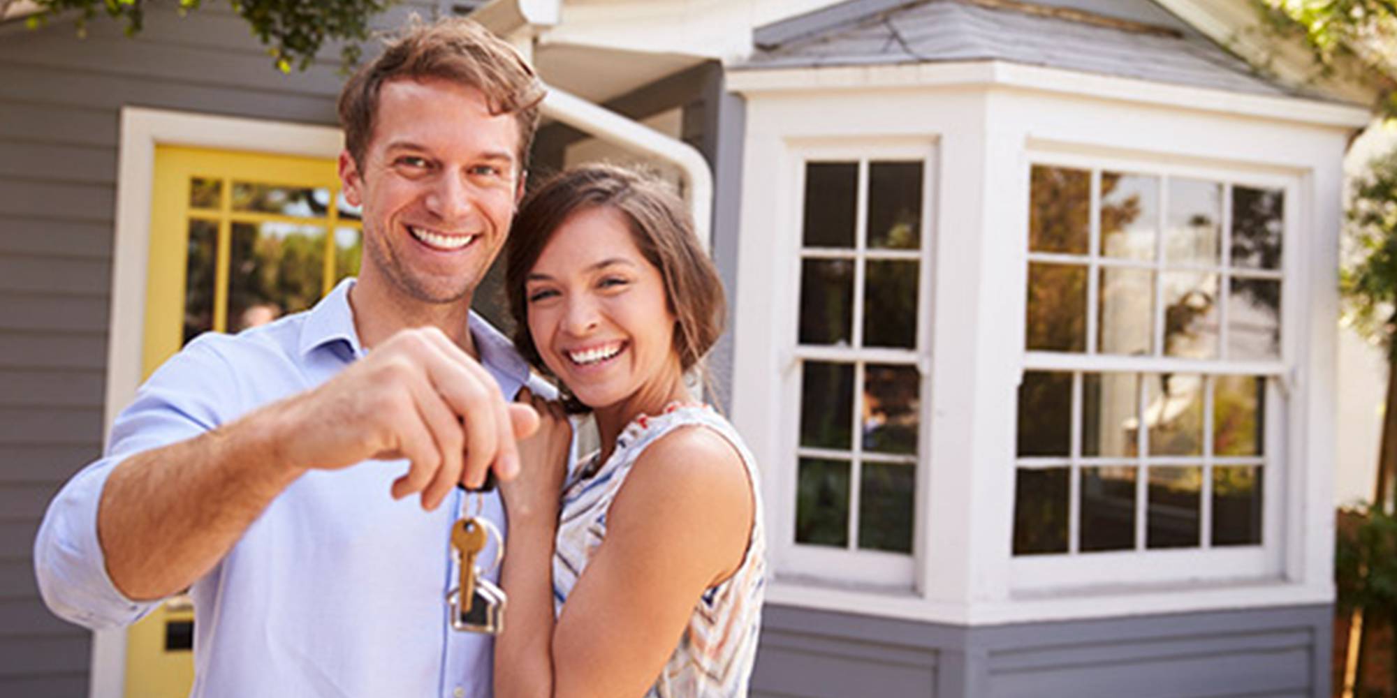 A young couple holding a house key in front of their home.